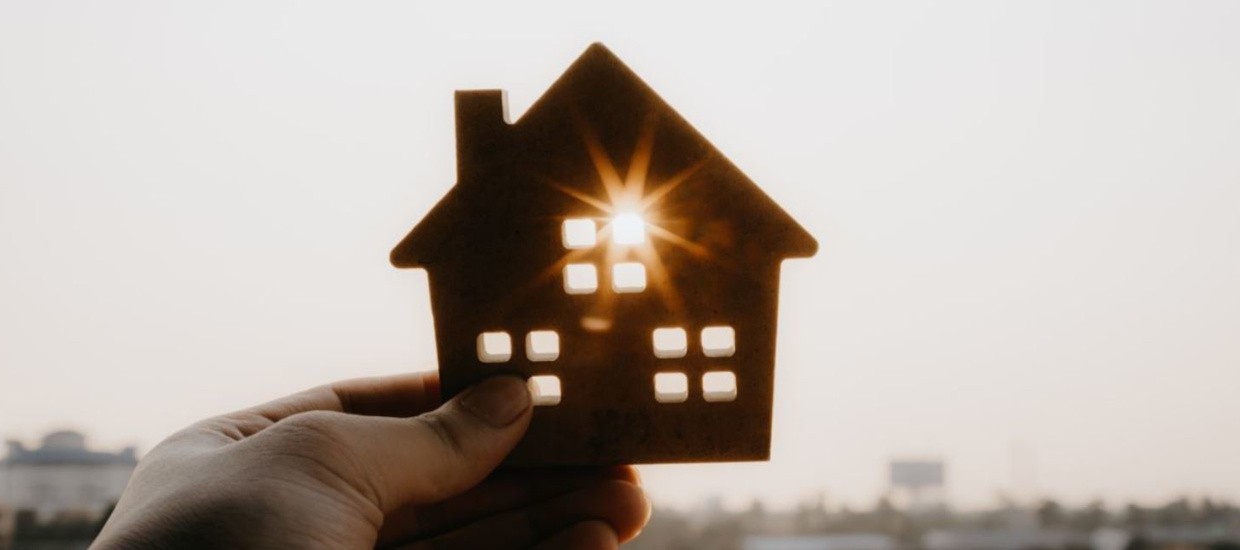 hand holding cutout of a house up to sun