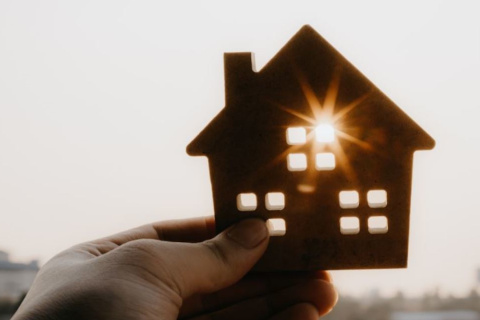 hand holding cutout of a house up to sun